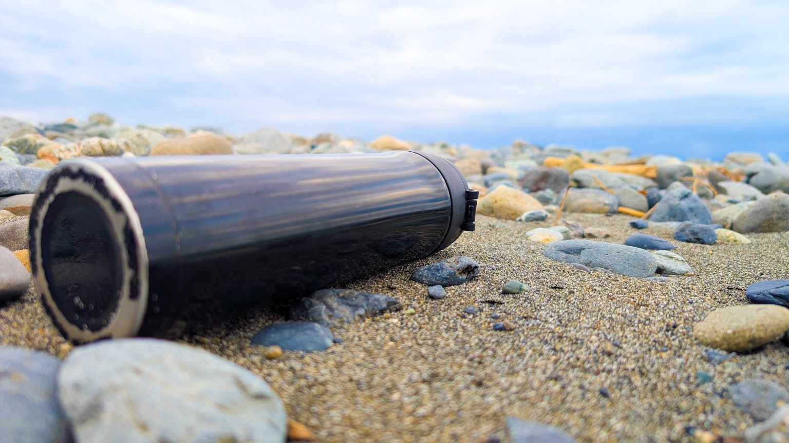 Bình giữ nhiệt đen nằm trên bãi biển cát giữa những viên sỏi