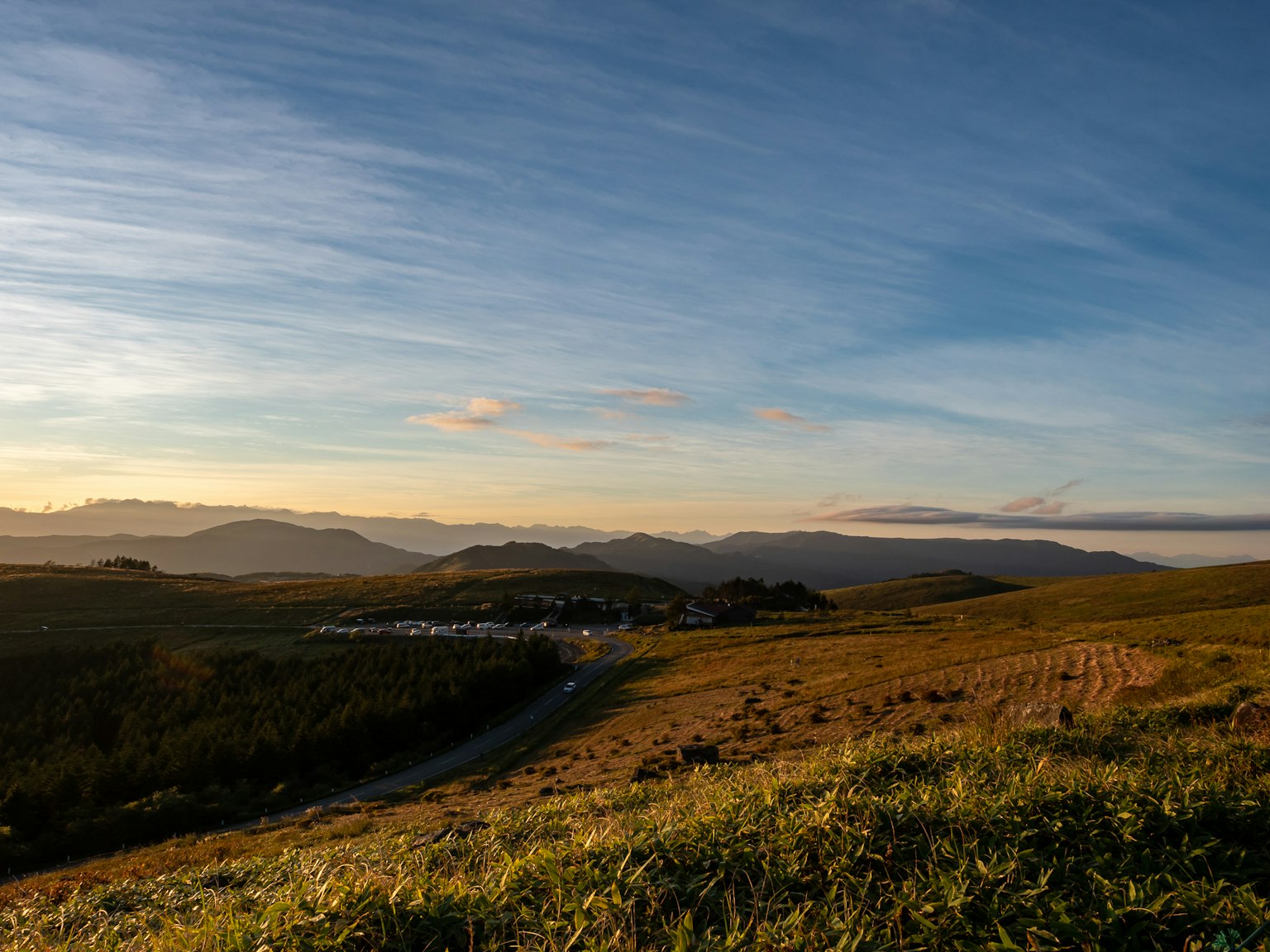 Tranquil landscape at dusk featuring green fields and distant mountains