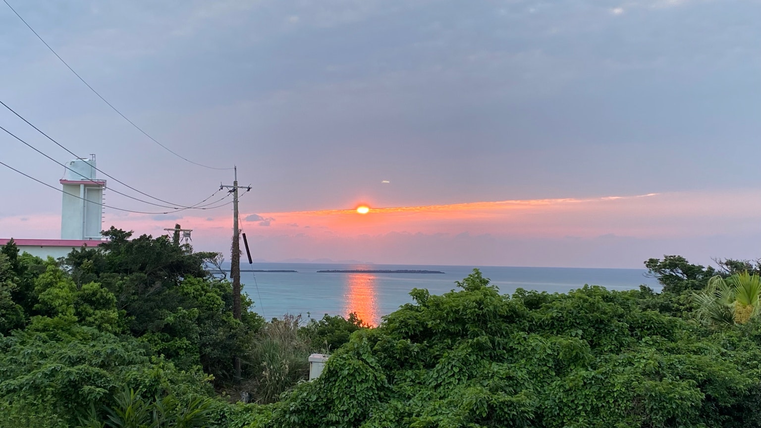 Landscape featuring a sunset over the sea with lush greenery