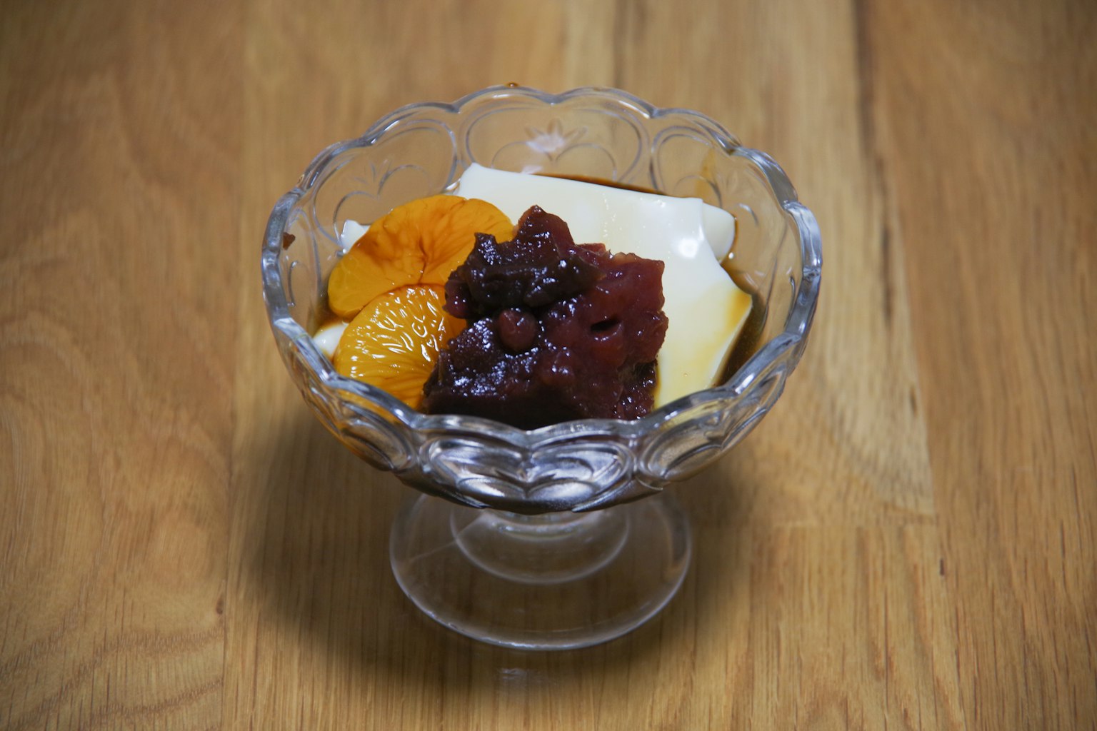 Postre en un tazón de vidrio con crema blanca pasta de frijoles rojos y rodajas de naranja