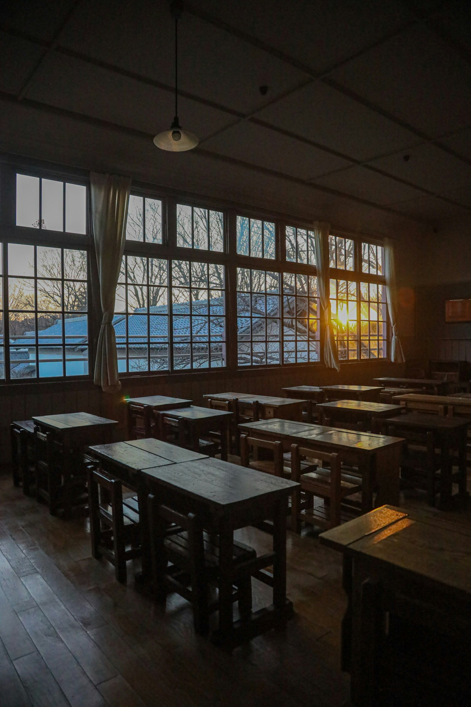 Aula con banchi e sedie in legno illuminati dal tramonto attraverso grandi finestre
