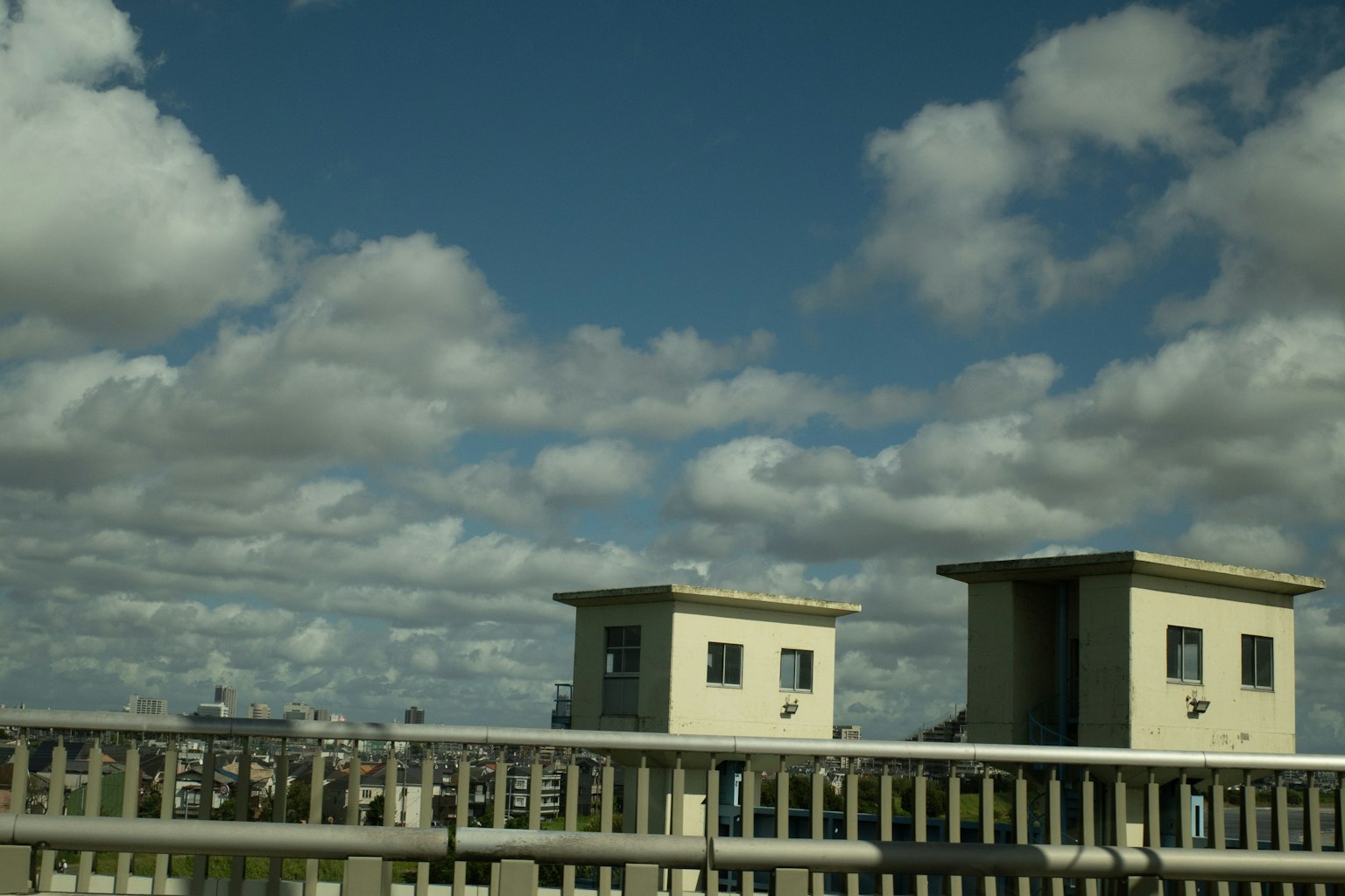 Two buildings under a blue sky with fluffy clouds and a bridge