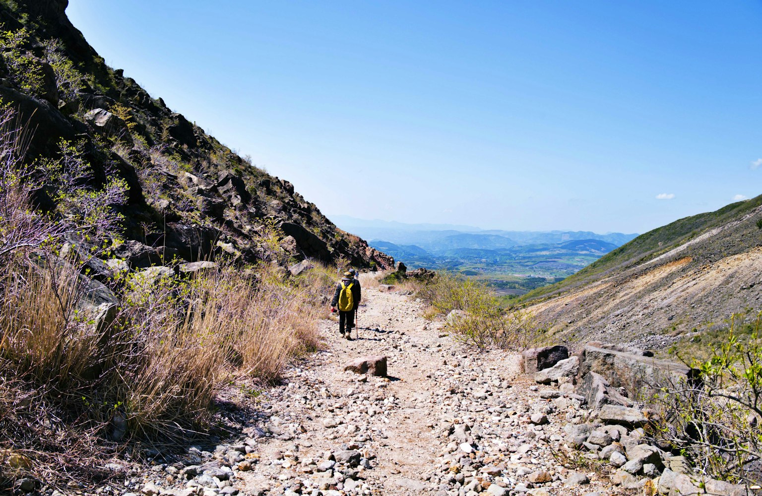 Excursionista caminando por un sendero montañoso rocoso con vista escénica