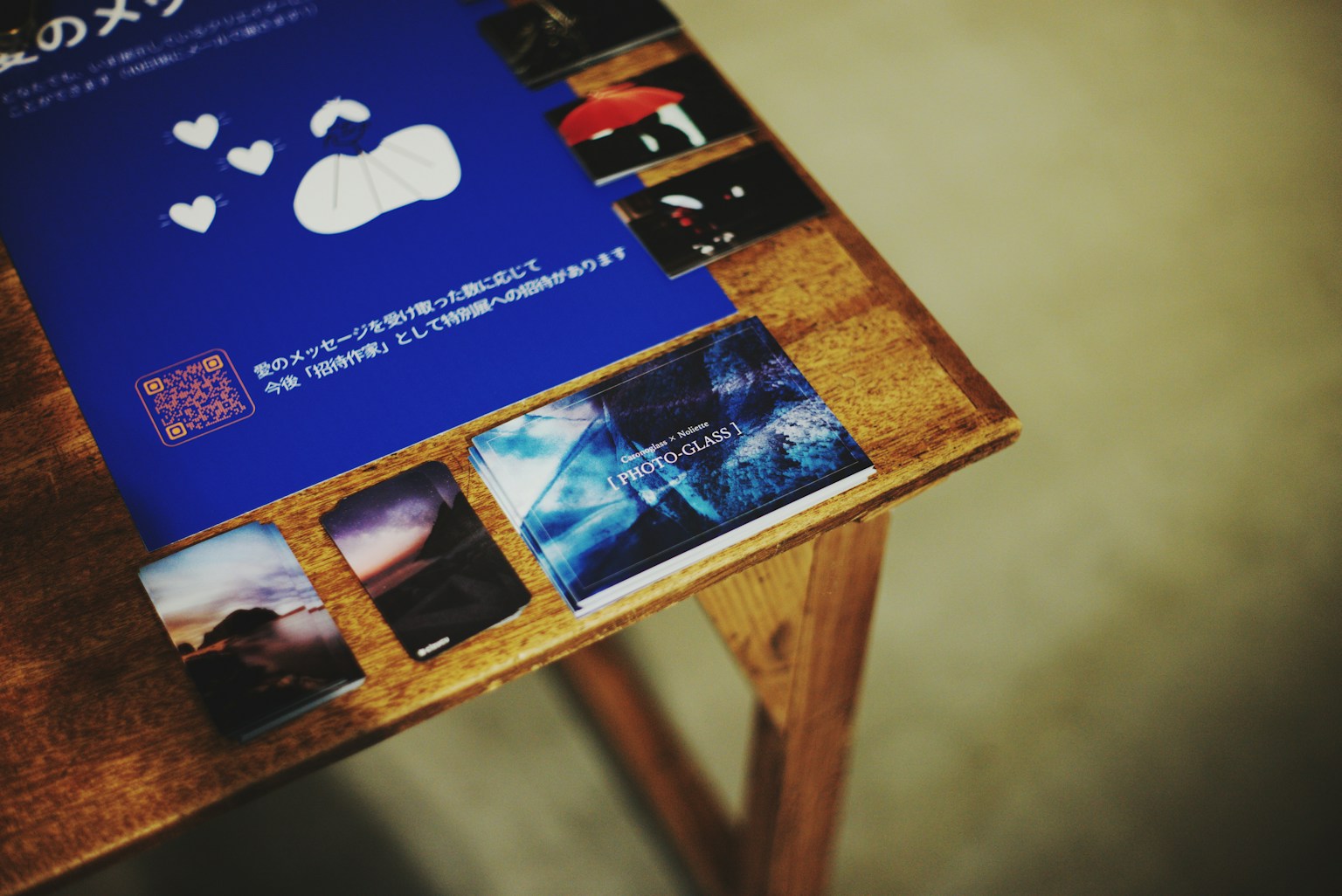 青い背景に白い雲の形が描かれたポスターと写真が並ぶ木製のテーブル