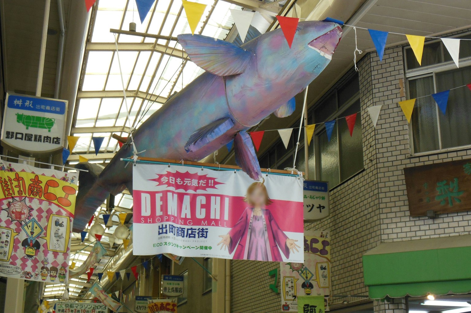 Modelo de pez gigante colgado del techo en una calle comercial con banderas coloridas