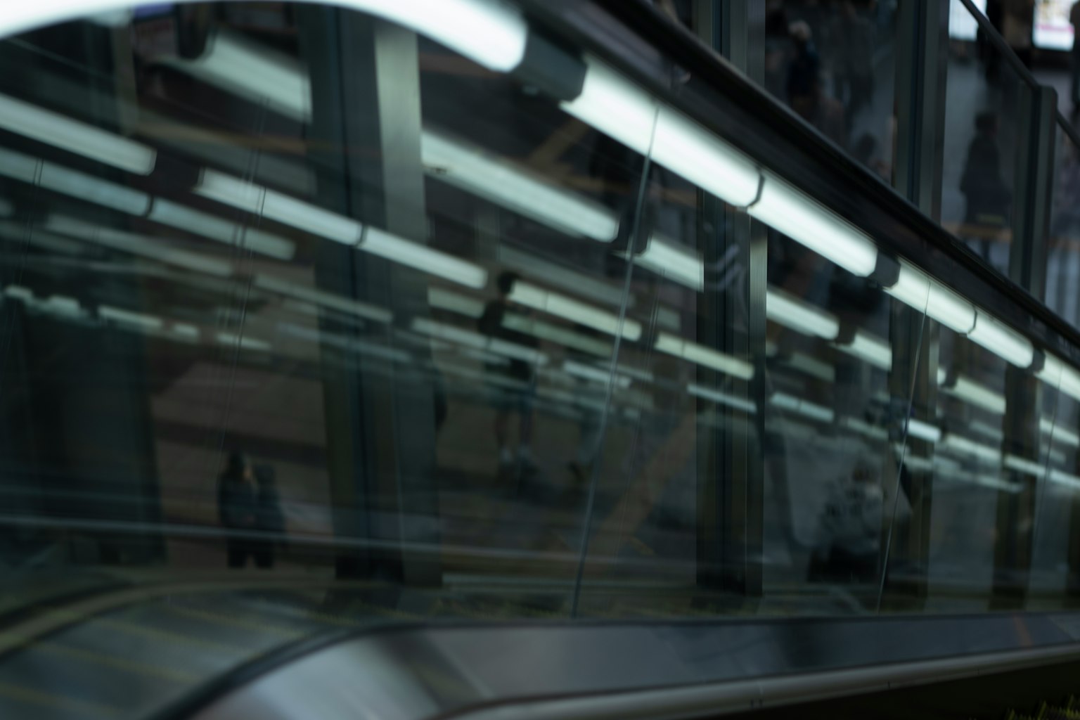 Scène urbaine capturée près d'un escalator avec des reflets des lumières au-dessus