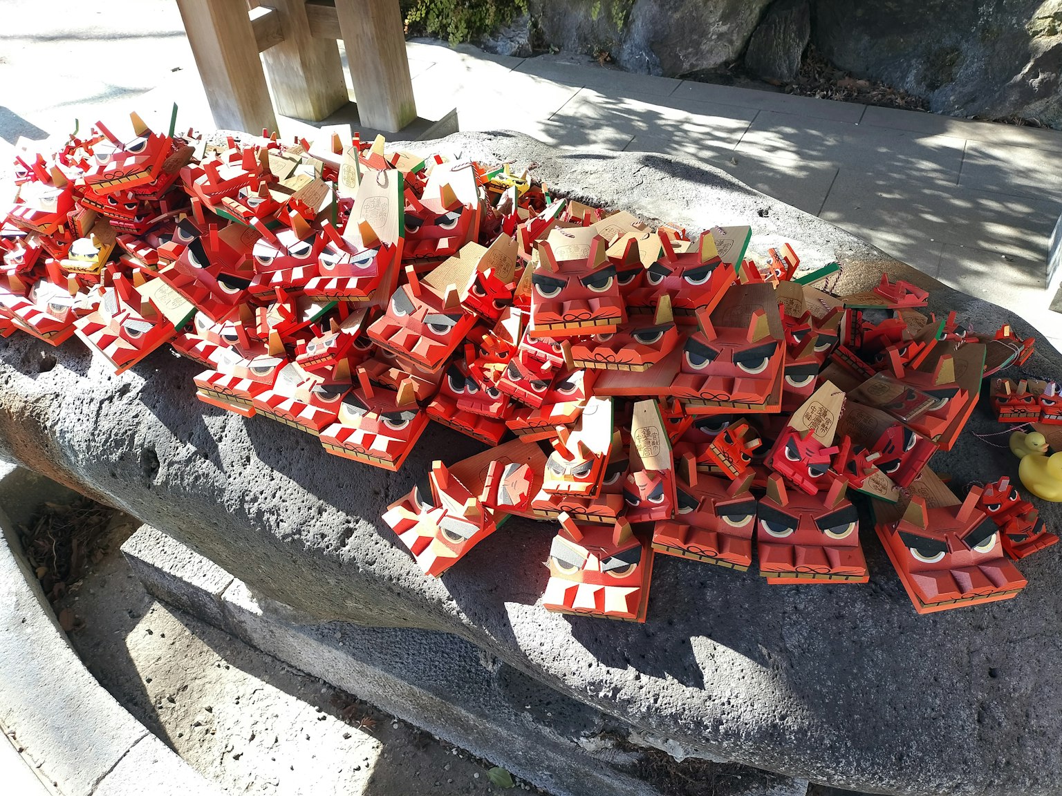 Une grande collection de masques en bois rouges avec des visages féroces disposés sur une surface en pierre