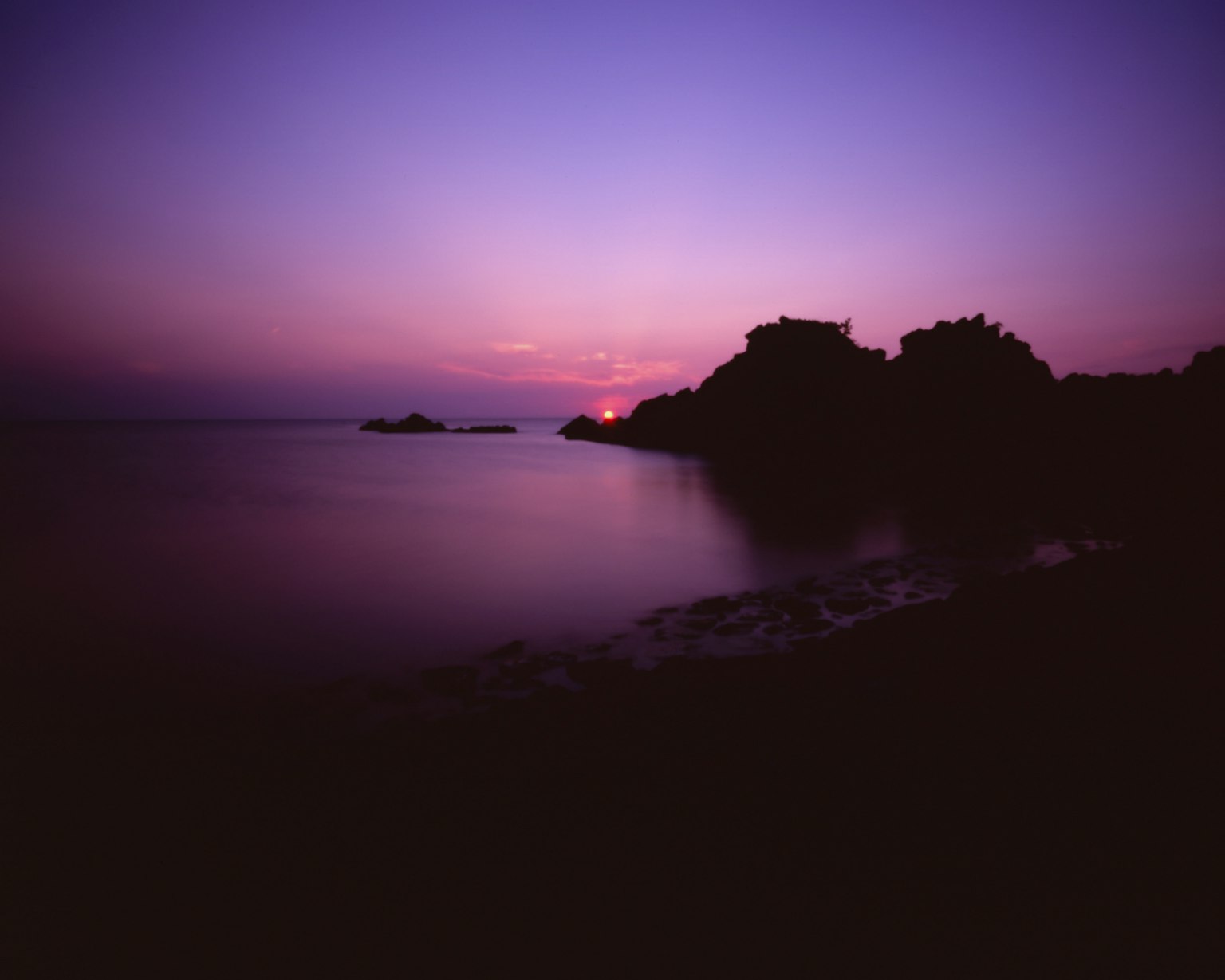 Paysage marin serein au coucher du soleil avec un ciel violet et des rochers en silhouette