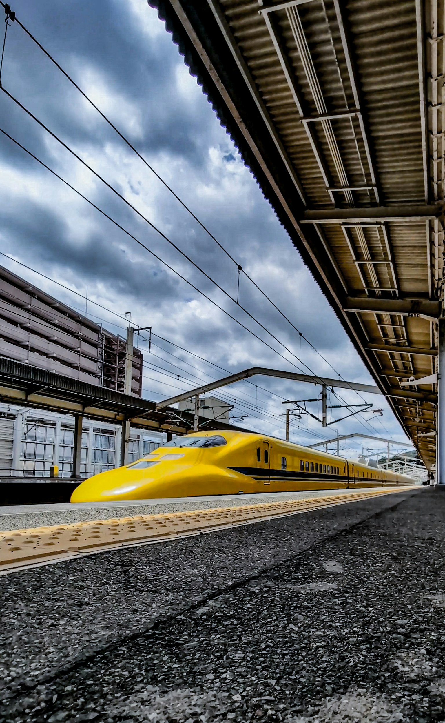A yellow Shinkansen train at a station platform under dramatic clouds