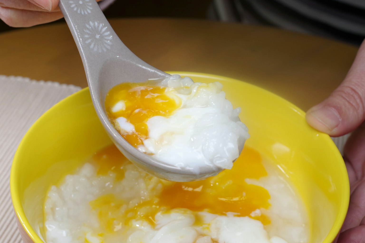 Una mano sosteniendo una cuchara con gachas de arroz cubiertas con yema de huevo
