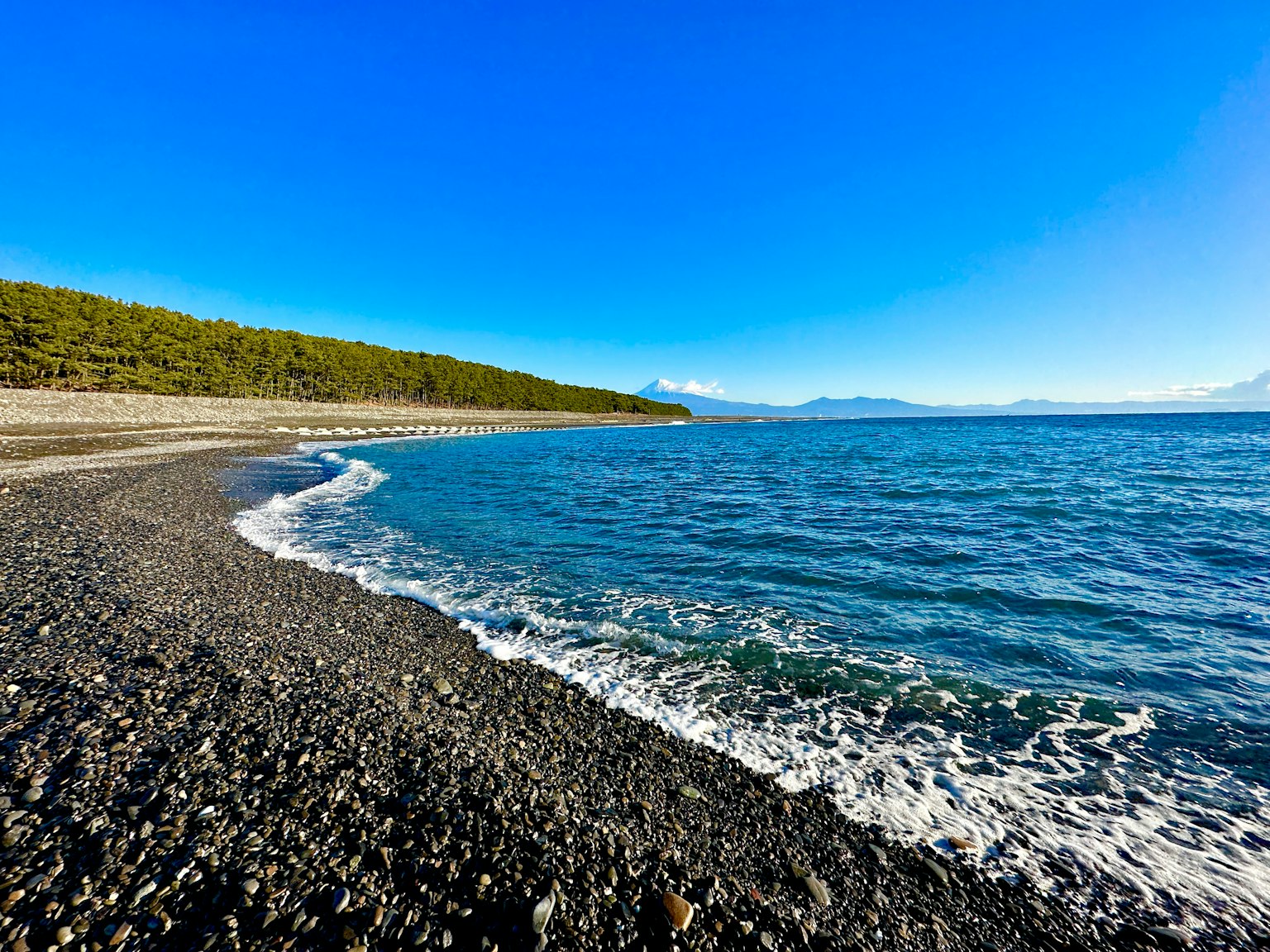 Landschaftsansicht eines Kiesstrandes unter einem hellblauen Himmel mit ruhigen Ozeanwellen