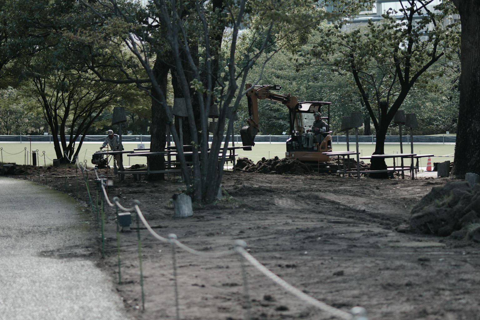 Baustelle in einem Park mit sichtbaren Maschinen und Arbeitern grüne Bäume und aufgewühlte Erde