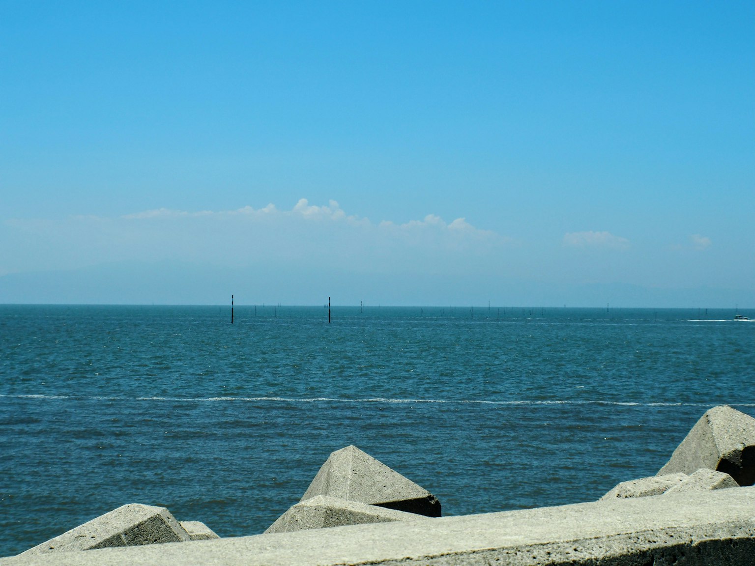 Scenic view of blue ocean and clear sky with rocky breakwater in foreground and wind turbines in the distance