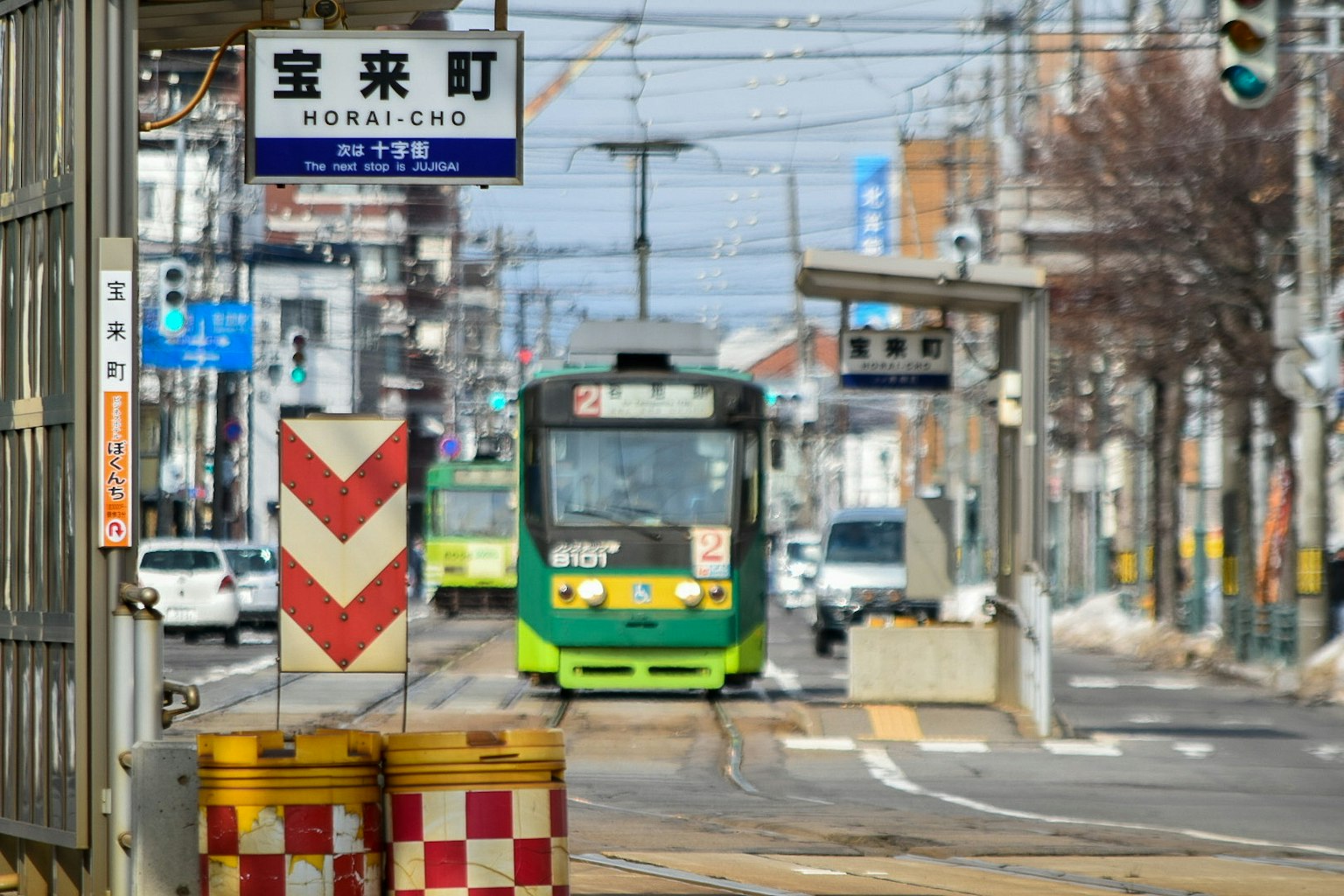 Fermata del tram Horai-cho con un tram verde e un paesaggio urbano