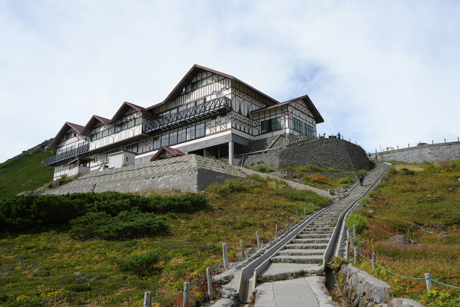 Large lodging building located on a hillside featuring green grass and stone steps