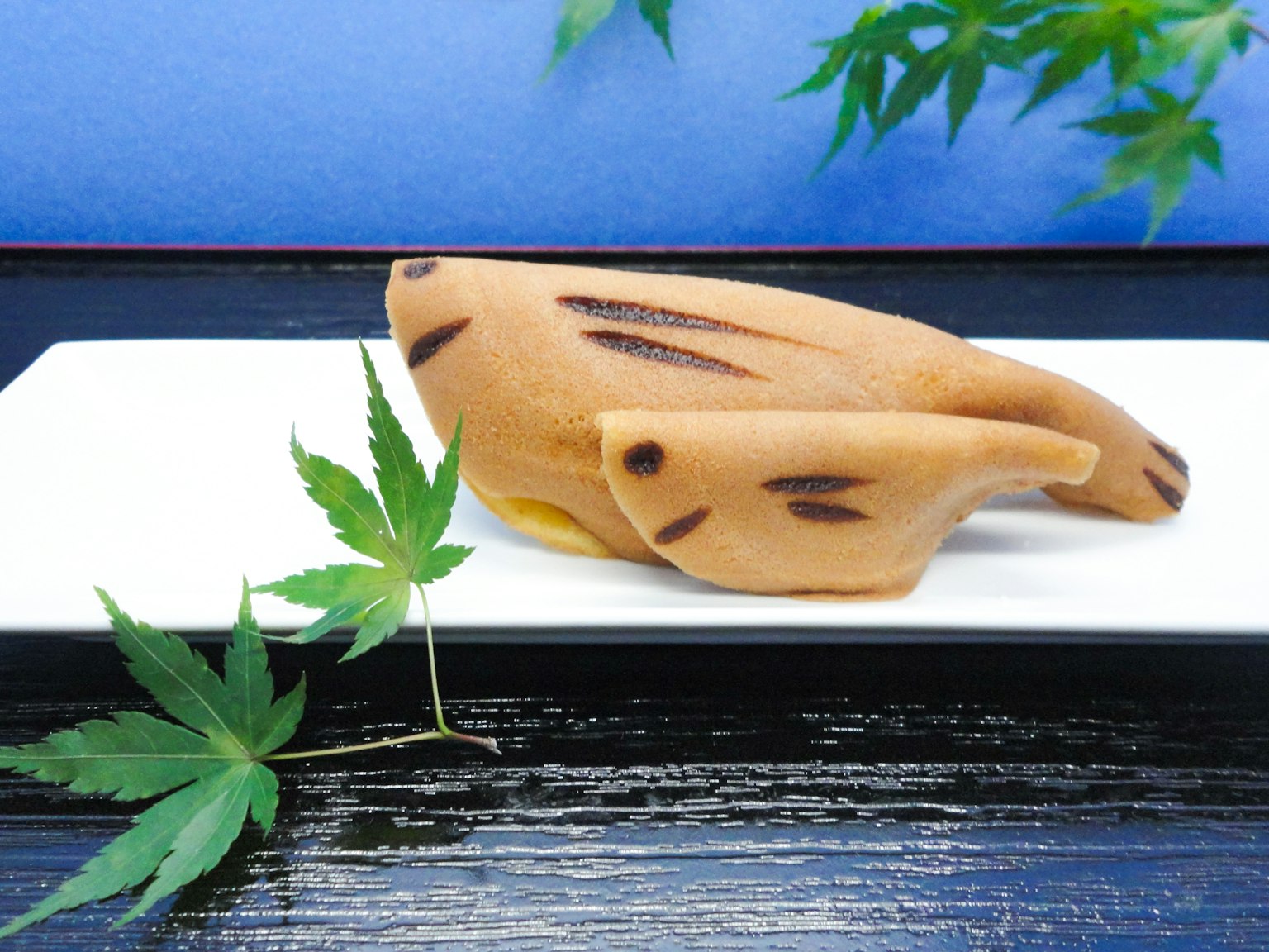 Wagashi a forma di foglia posato su un piatto bianco con uno sfondo blu