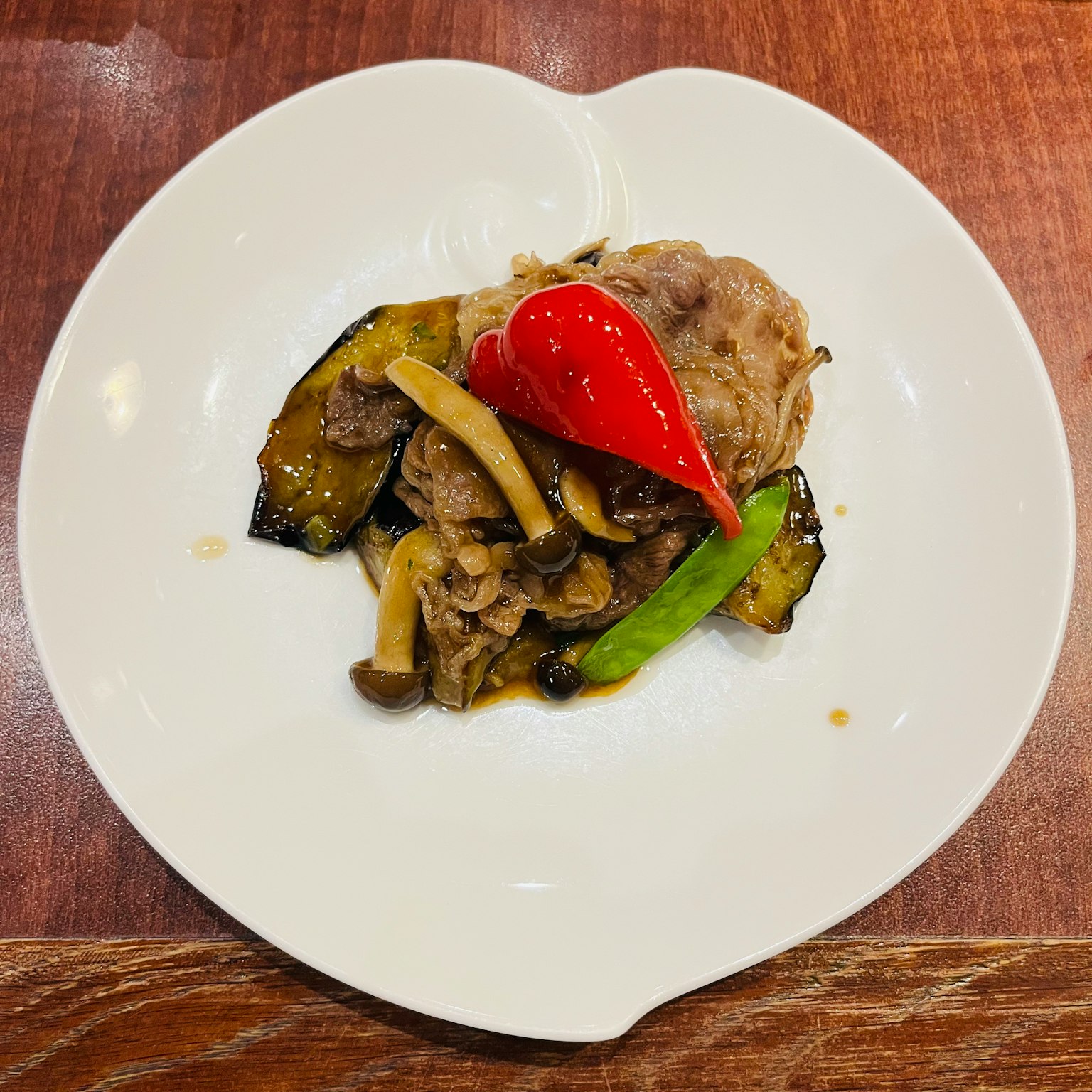 白色盘子里的肉和蔬菜菜肴，上面放着红辣椒