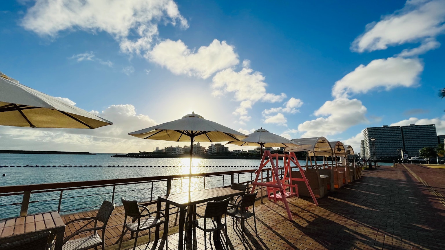 Terrasse de café en bord de mer avec des parasols sous un ciel bleu éclatant et le soleil