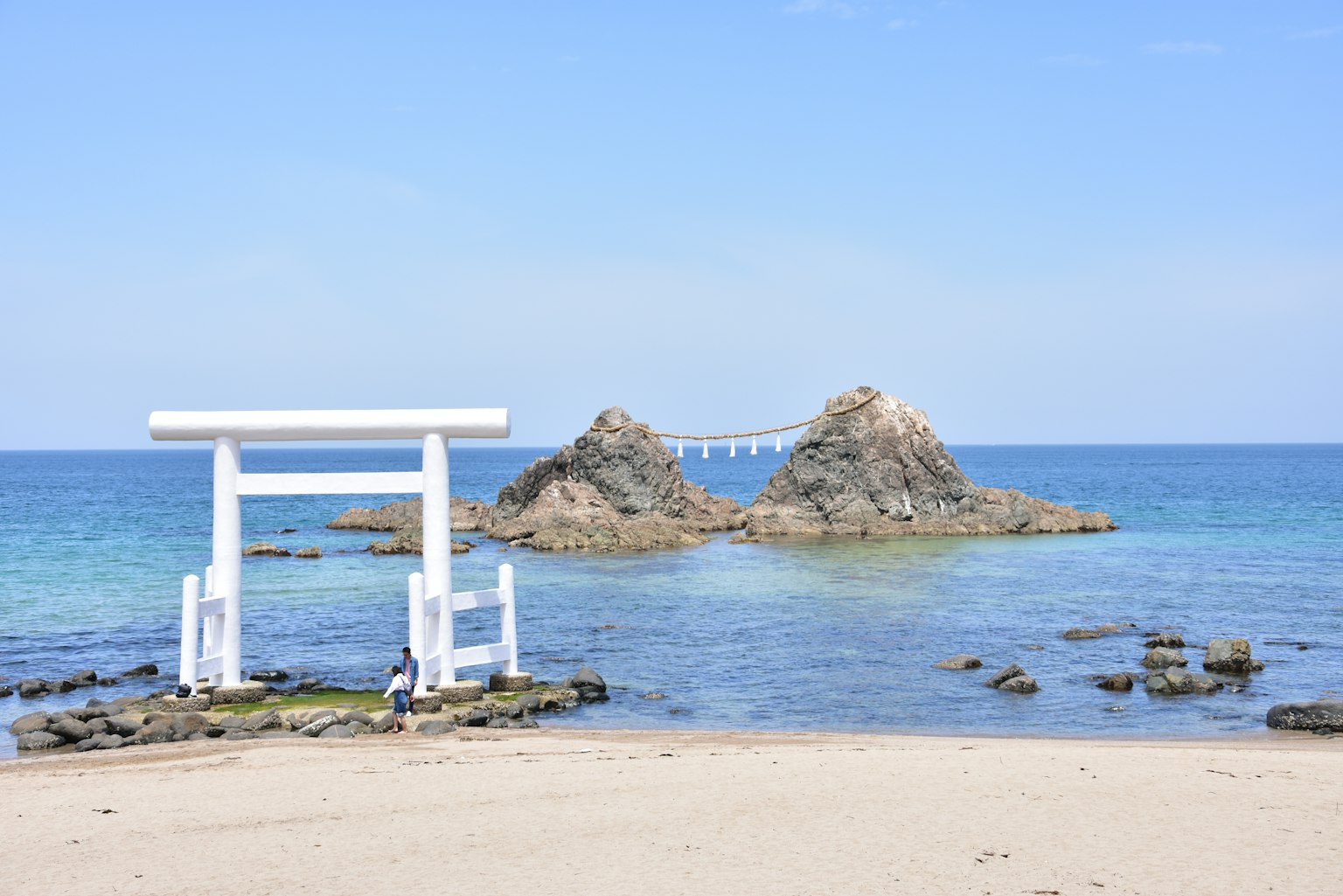 Vista panoramica di un torii bianco vicino alla spiaggia con due isole rocciose sullo sfondo