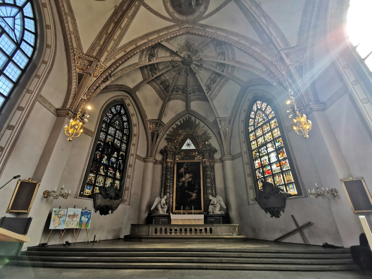 Interior de una iglesia con luz brillante que entra por vitrales coloridos y figuras esculpidas a cada lado del altar