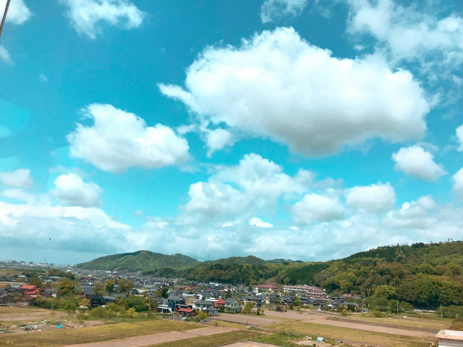 A landscape featuring a blue sky with white clouds above a small town and mountains