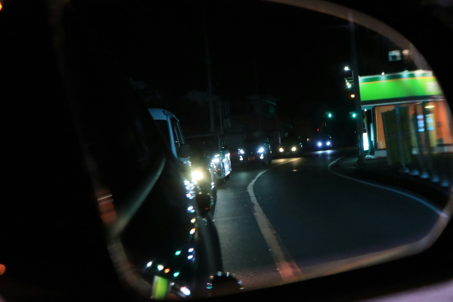 Riflessione di auto su una strada tortuosa di notte in uno specchietto laterale
