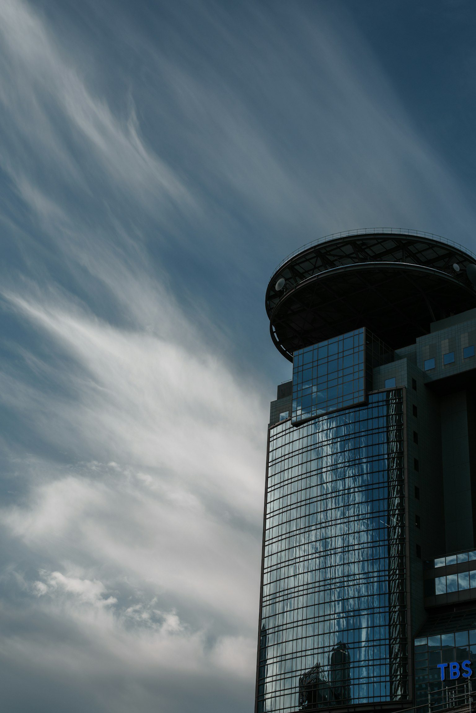 Side view of a skyscraper with a glass facade and unique rooftop design