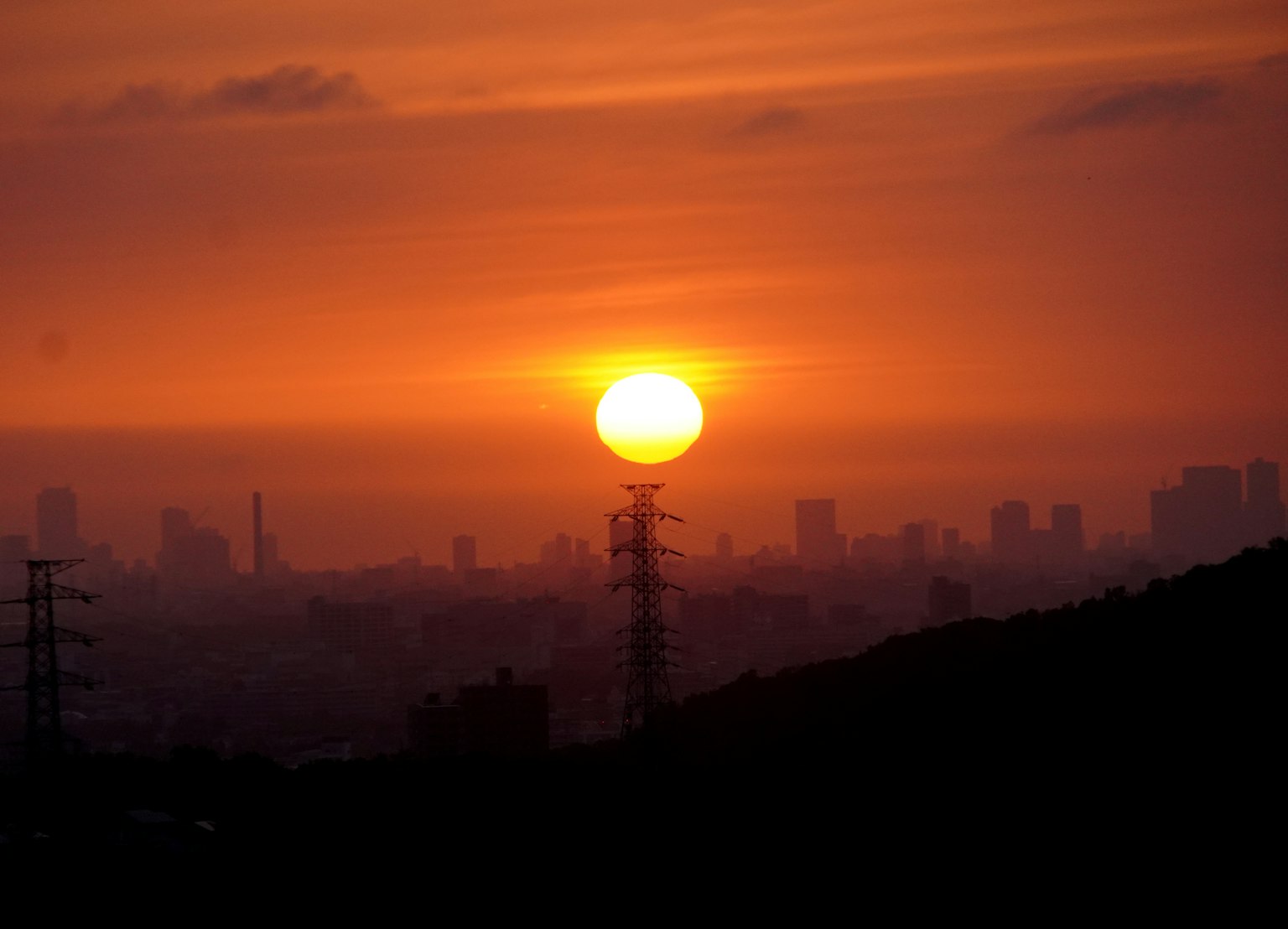 Atardecer sobre un horizonte urbano con siluetas y líneas eléctricas