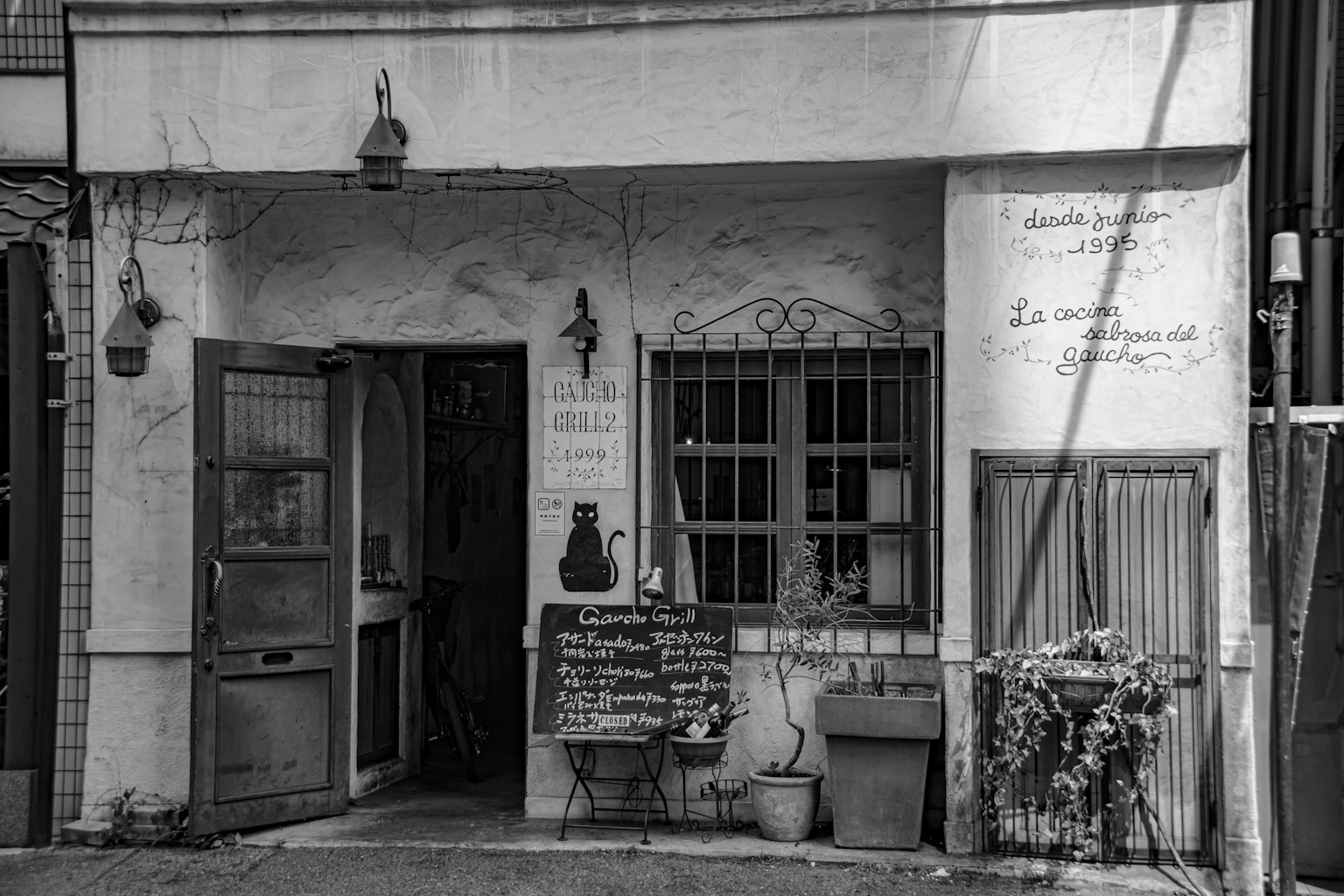 Piccolo edificio con esterno in bianco e nero caratterizzato da una porta in ferro e finestre distintive una lavagna con il menu esposto