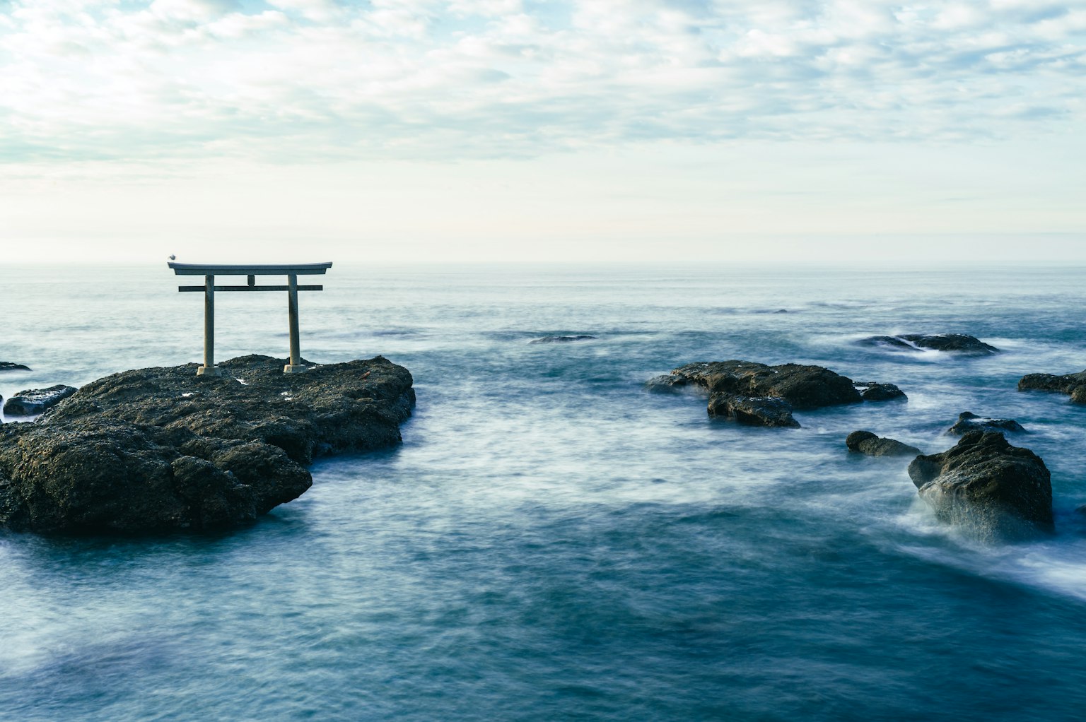 Torii gate on rocky shore with ocean waves