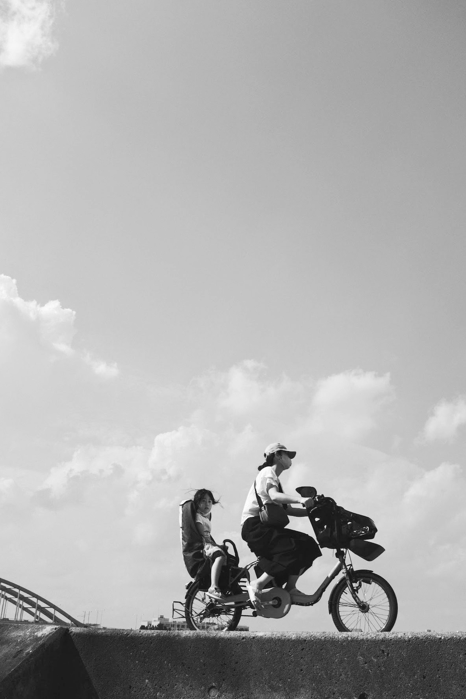 Schwarzweißfoto von Eltern und Kind auf einem Fahrrad unter blauem Himmel und Wolken