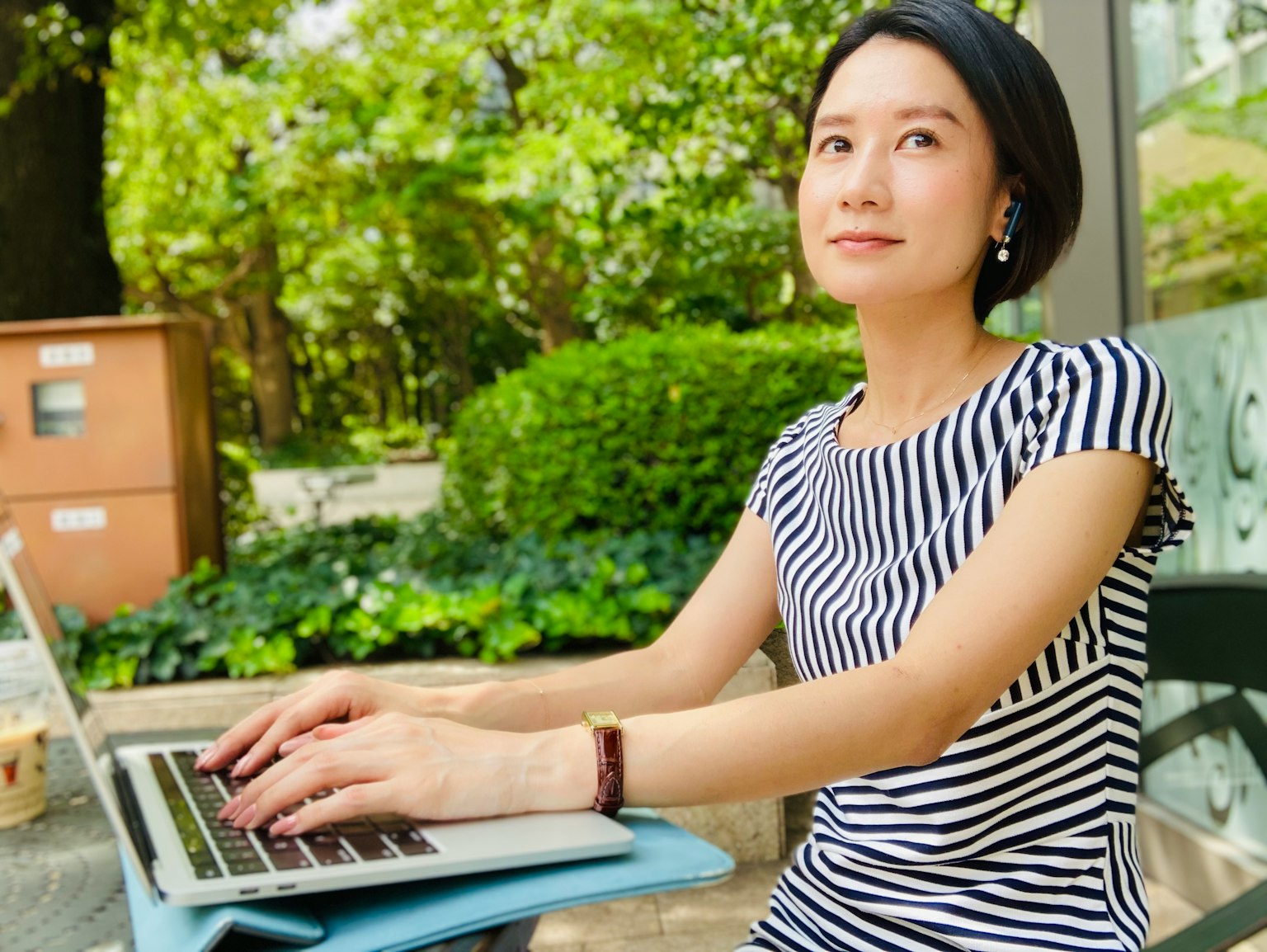 Frau, die in einem Park einen Laptop benutzt, trägt ein gestreiftes Kleid mit grünem Hintergrund