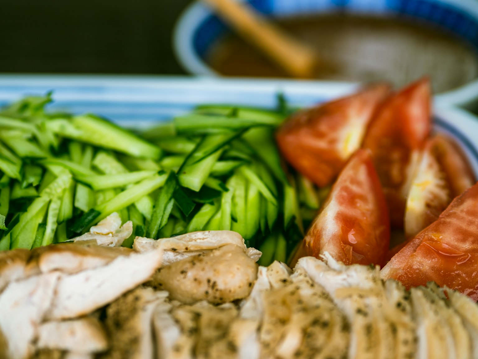 Photo de poulet tranché, concombre râpé et tomate disposés sur une assiette