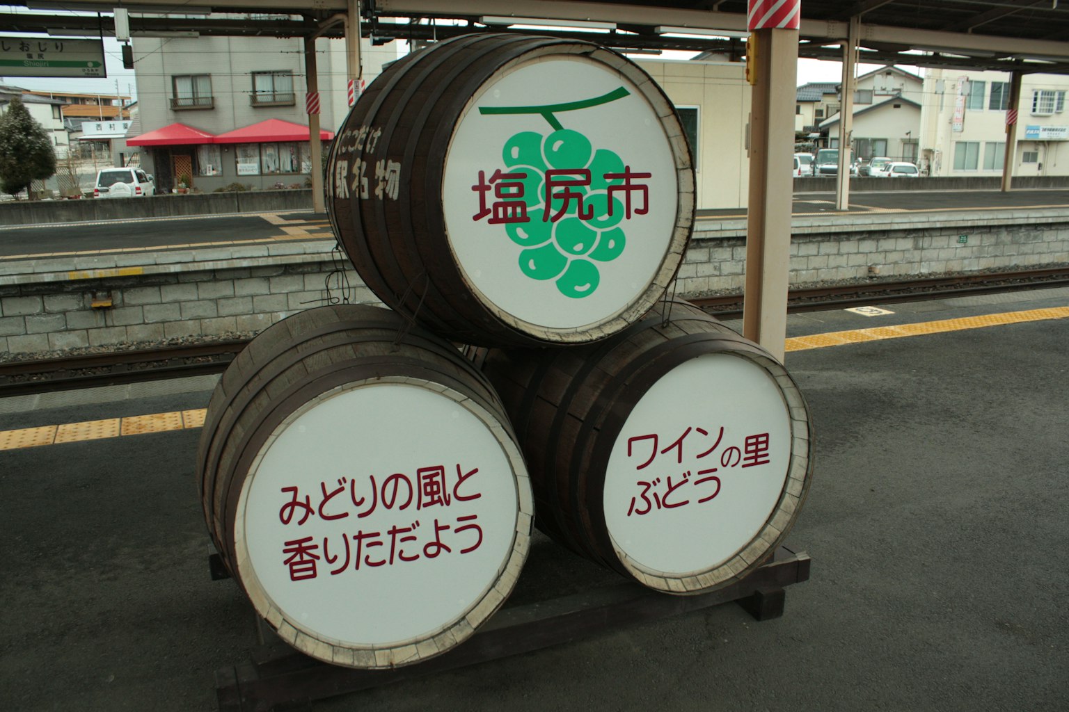 Tres barriles de madera en una plataforma de tren con ilustraciones de uvas y texto