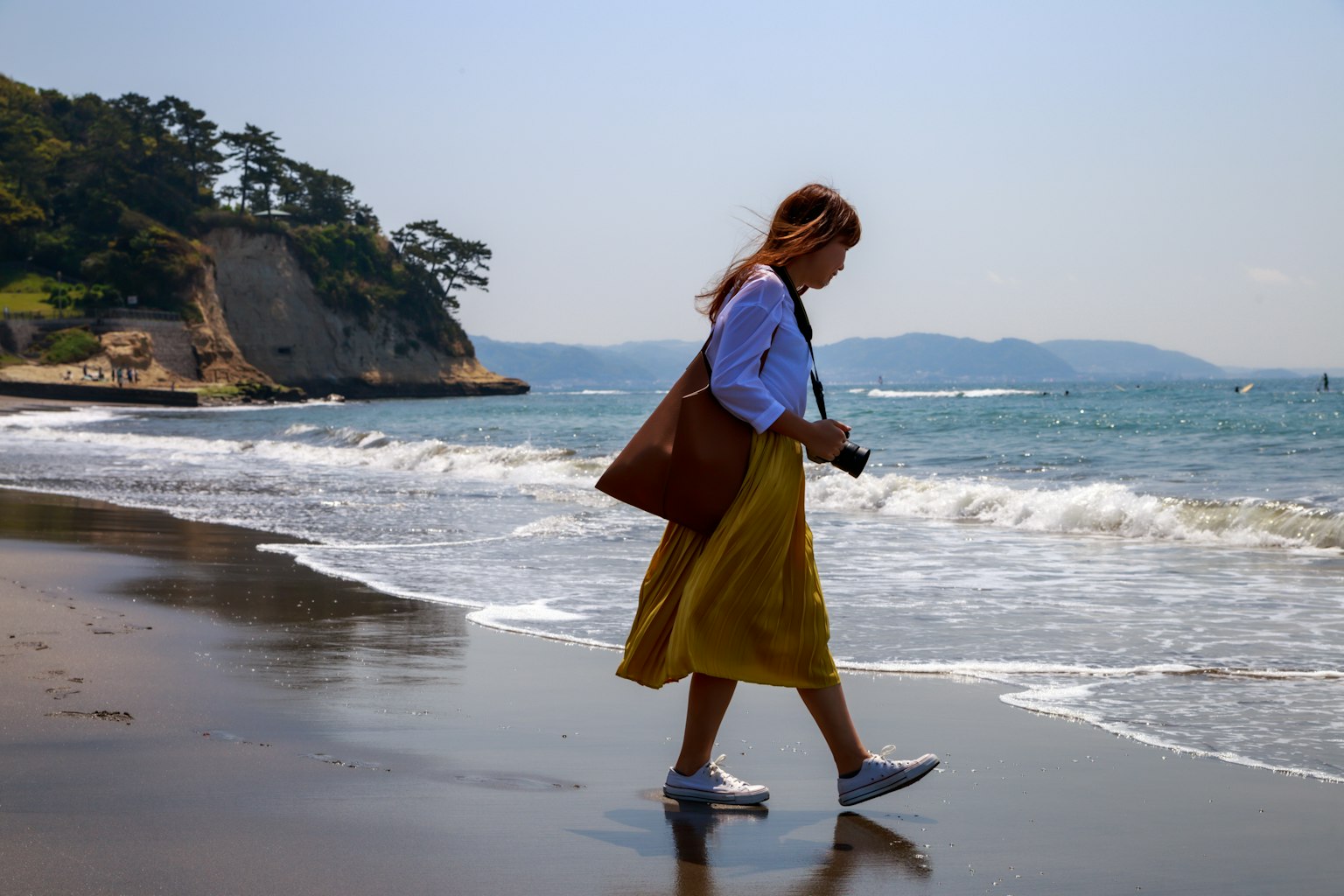 Woman walking on the beach holding a camera