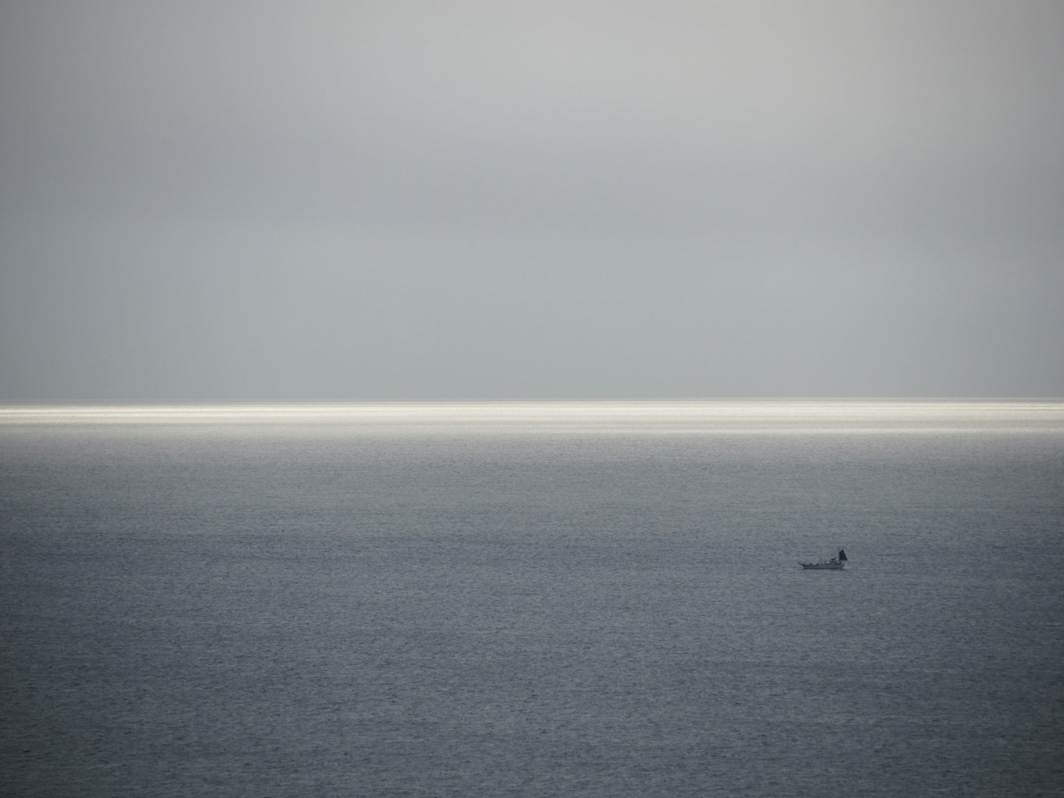 Una piccola barca che galleggia su un mare calmo sotto un cielo grigio tenue