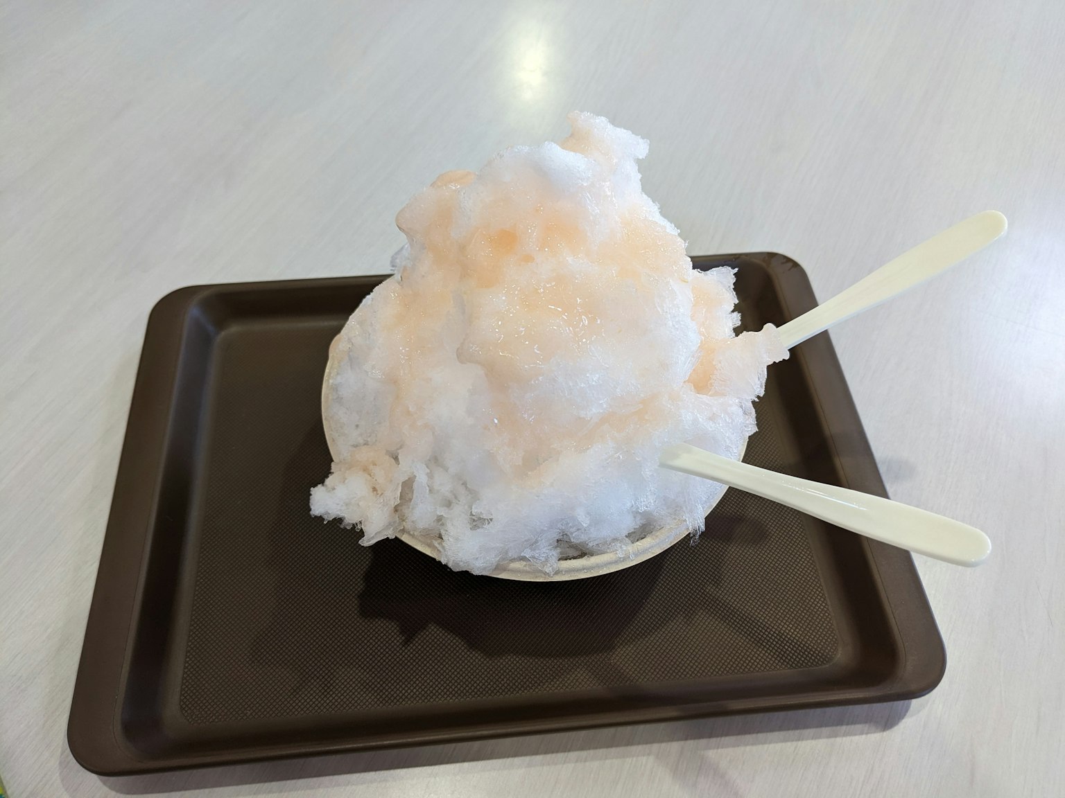 Shaved ice dessert topped with orange syrup served on a brown tray