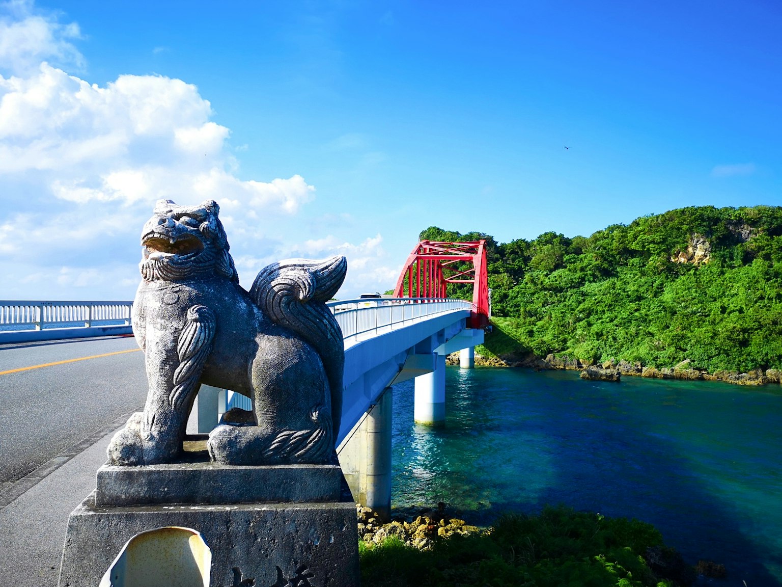 Estatua de león de piedra cerca de un puente con cielo azul y colinas verdes