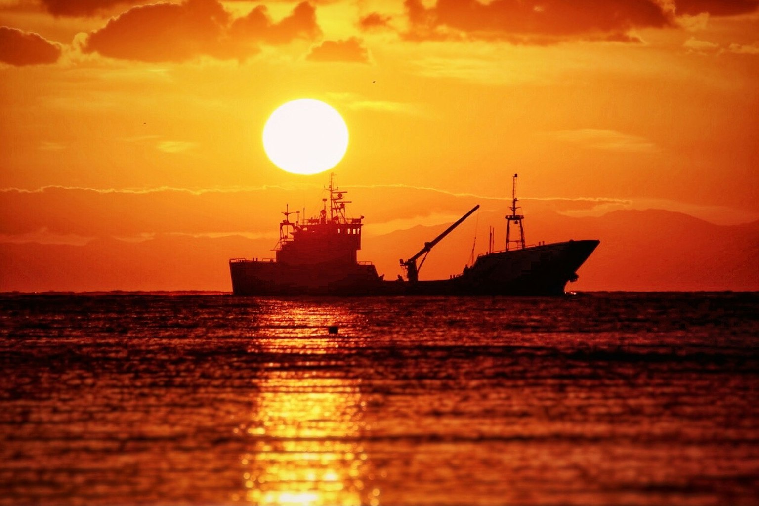 Silhouette di un peschereccio contro un tramonto che si riflette nell'oceano