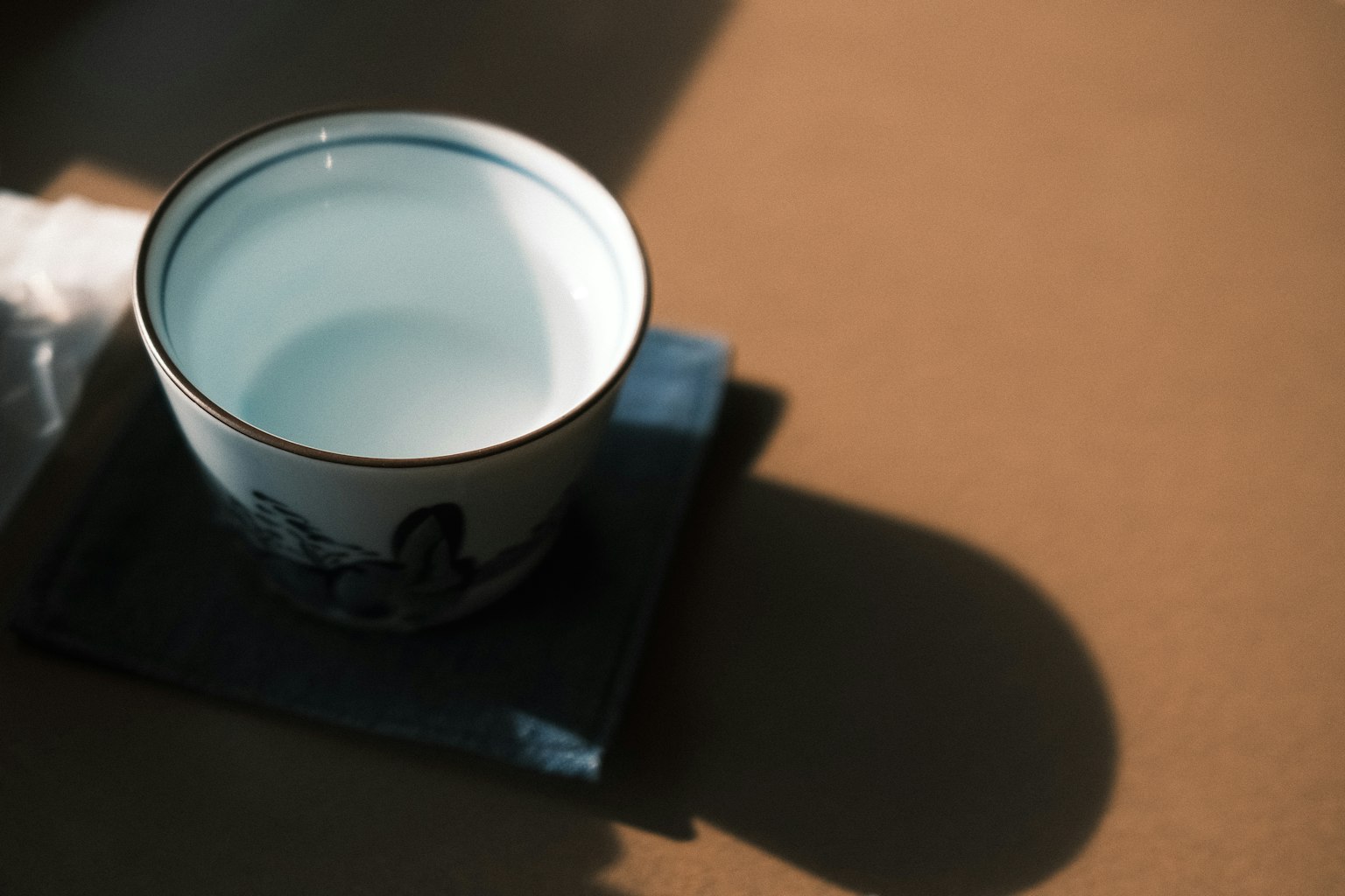 一个装有透明液体的杯子放在蓝色图案的碟子上，背景为棕色