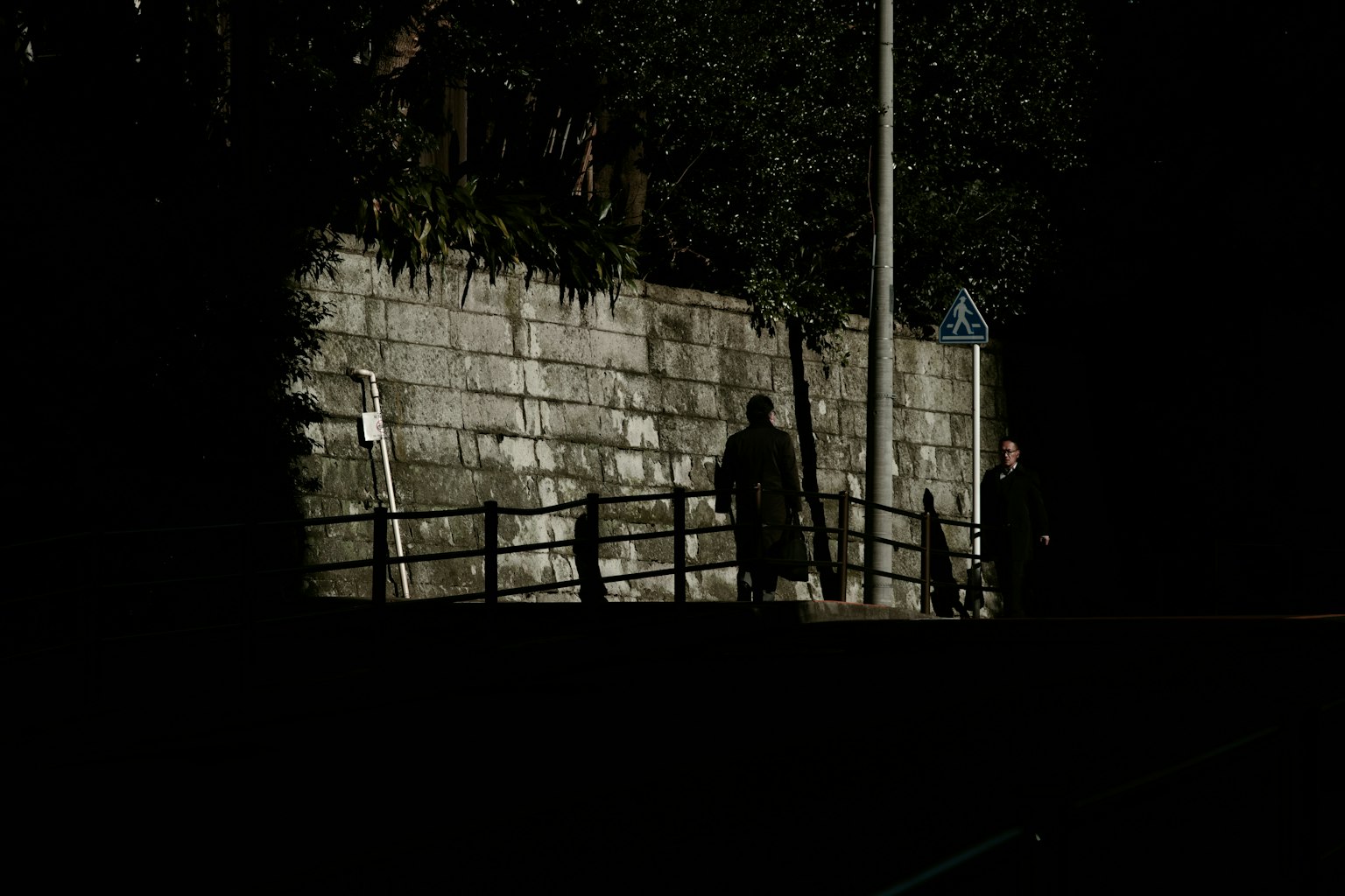 Silhouette di una persona che cammina davanti a un muro in una strada buia