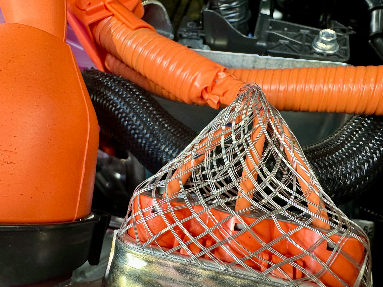 Primer plano de componentes del motor con mangueras naranjas y una estructura de malla metálica