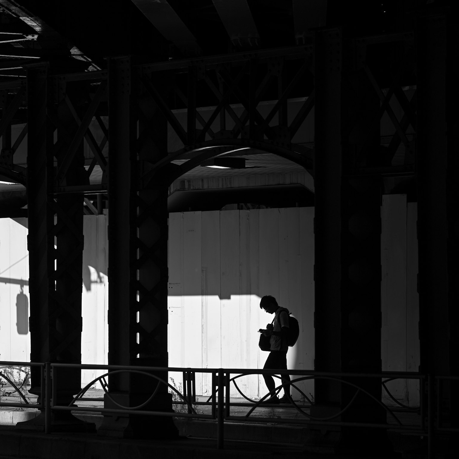 Silhouette of a person walking under a station structure in strong black and white contrast