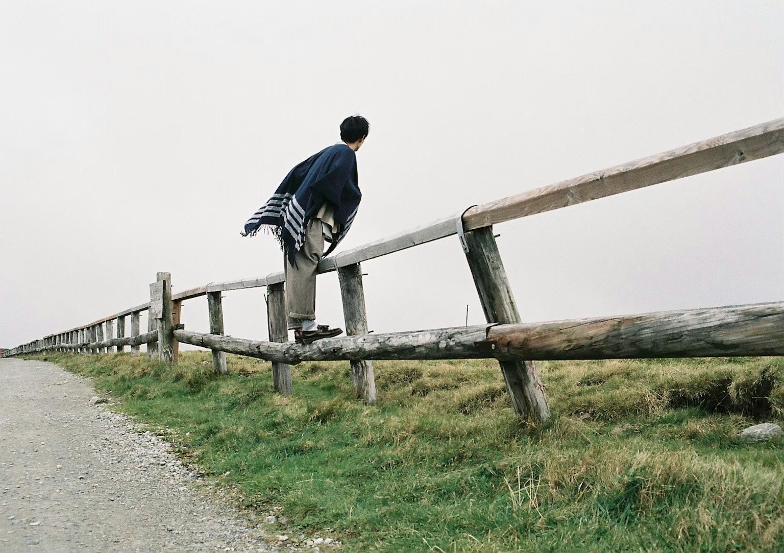A man leaning on a wooden fence with a natural landscape and cloudy sky