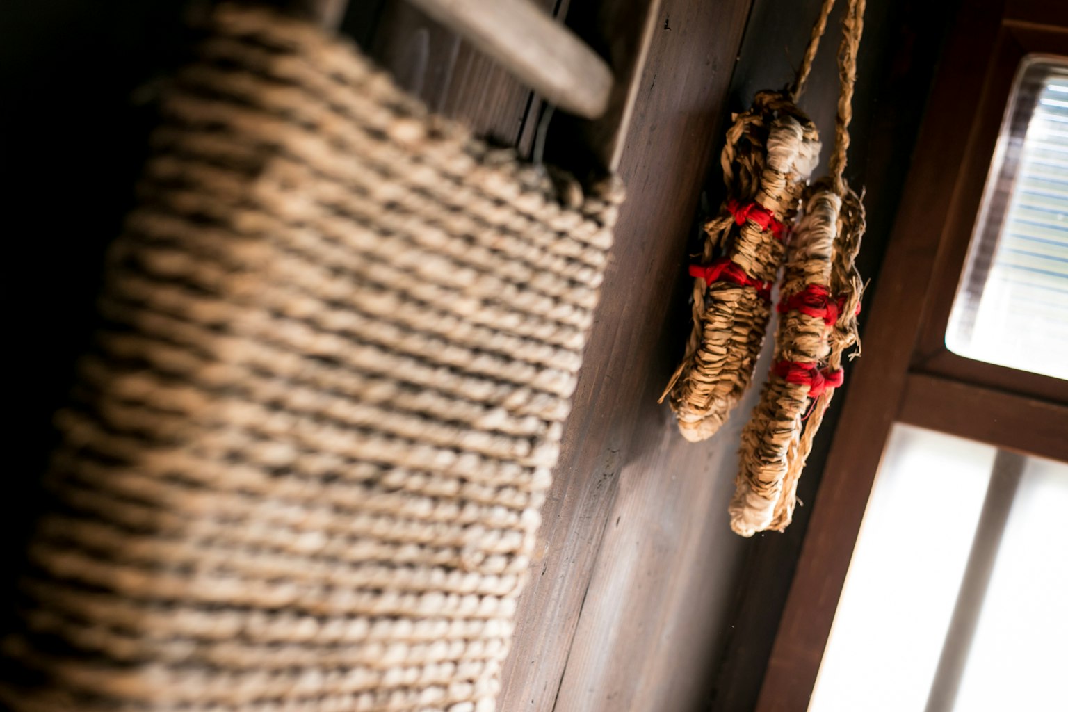 A woven wall hanging made of rope and bundles tied with red strings in a serene indoor setting