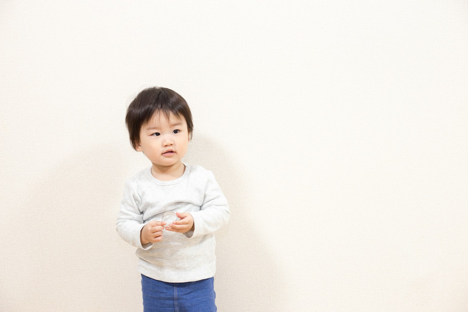 Bambino che sta in piedi davanti a un muro bianco con un maglione grigio e pantaloni blu