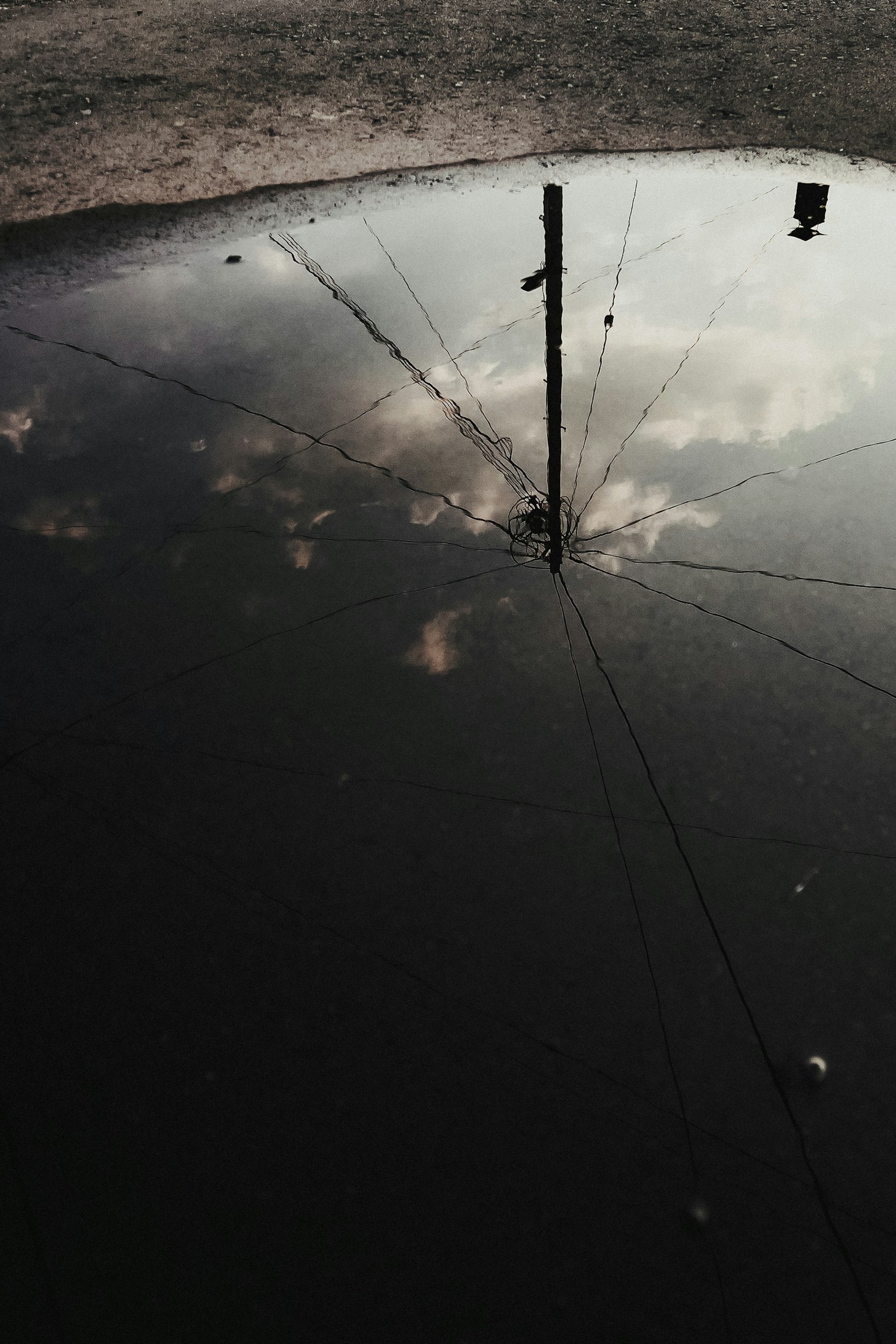 Reflexion von Wolken und einem Strommast in einer Pfütze