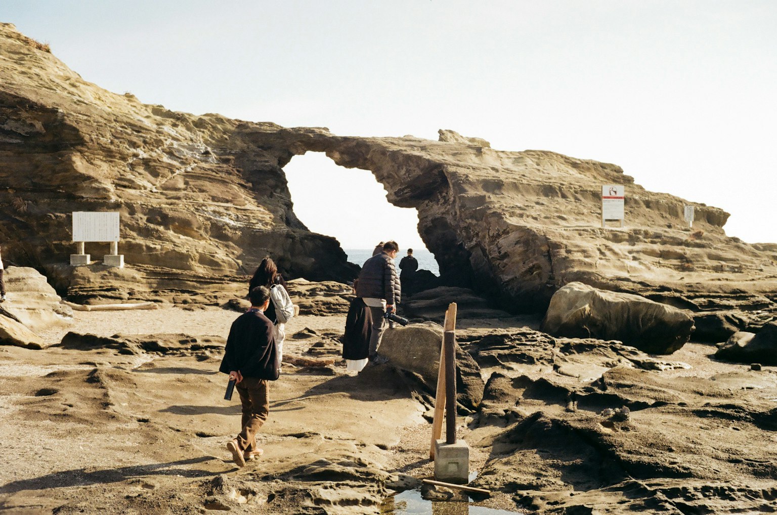 Personas caminando cerca de un arco de roca natural en una costa rocosa