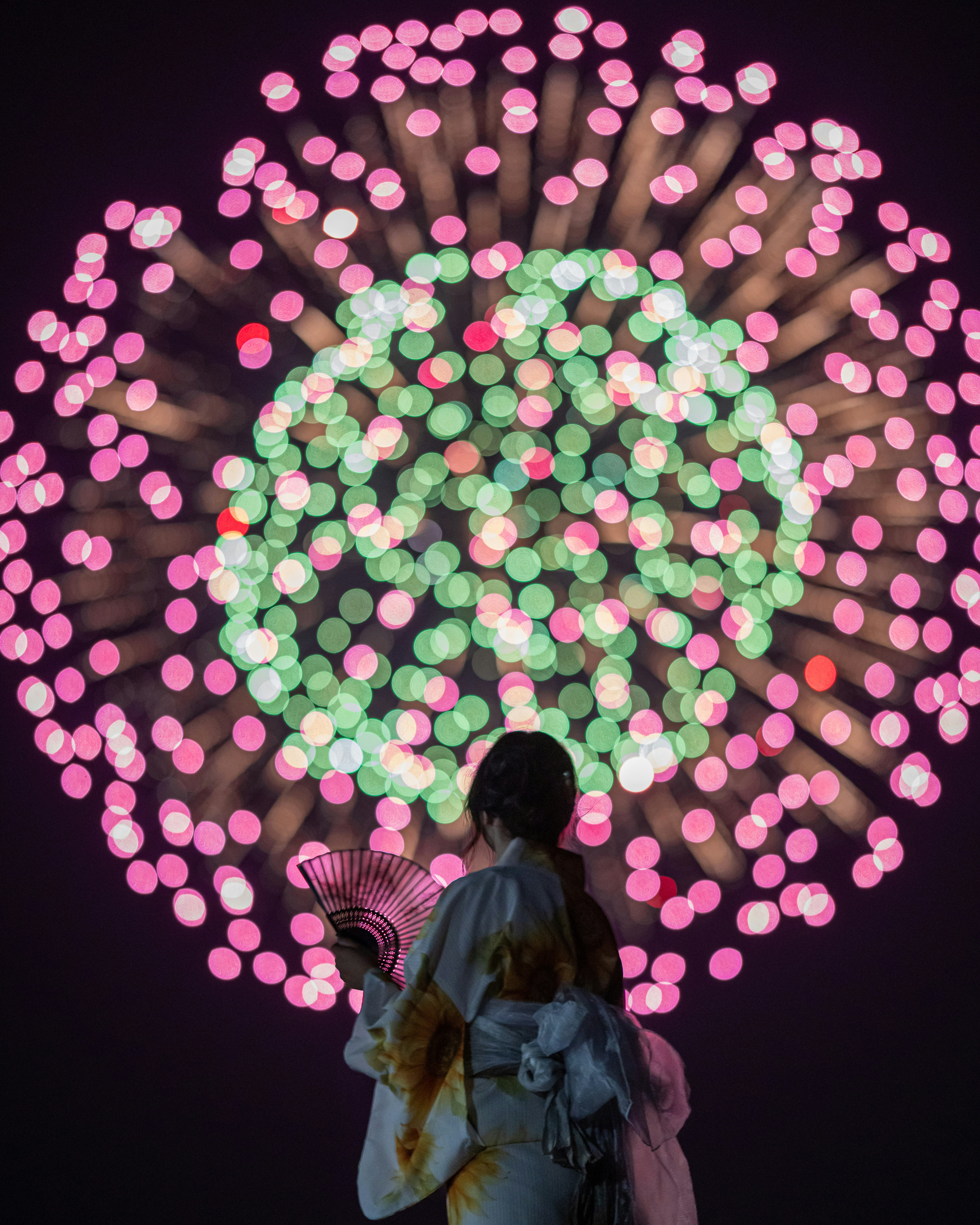 花火の玉ボケと扇子を持つ人の後ろ姿