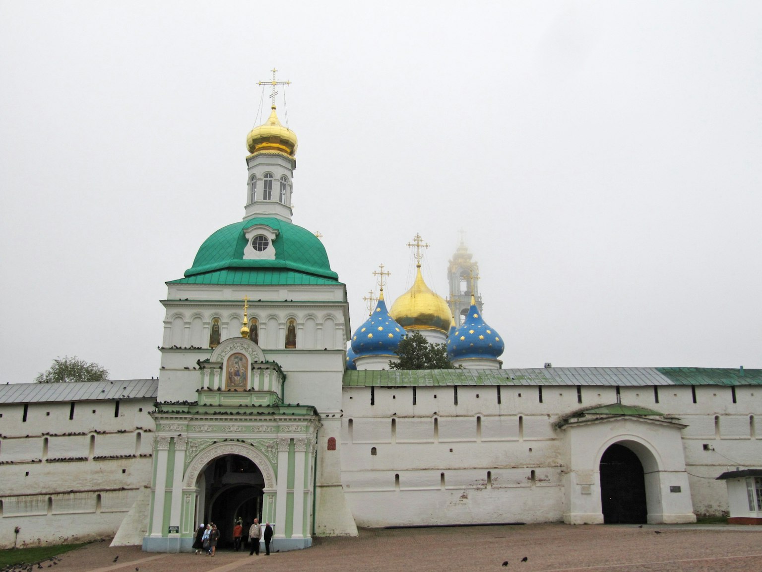 Foreground of a building with a green roof and golden crosses with a backdrop of blue and gold domed churches